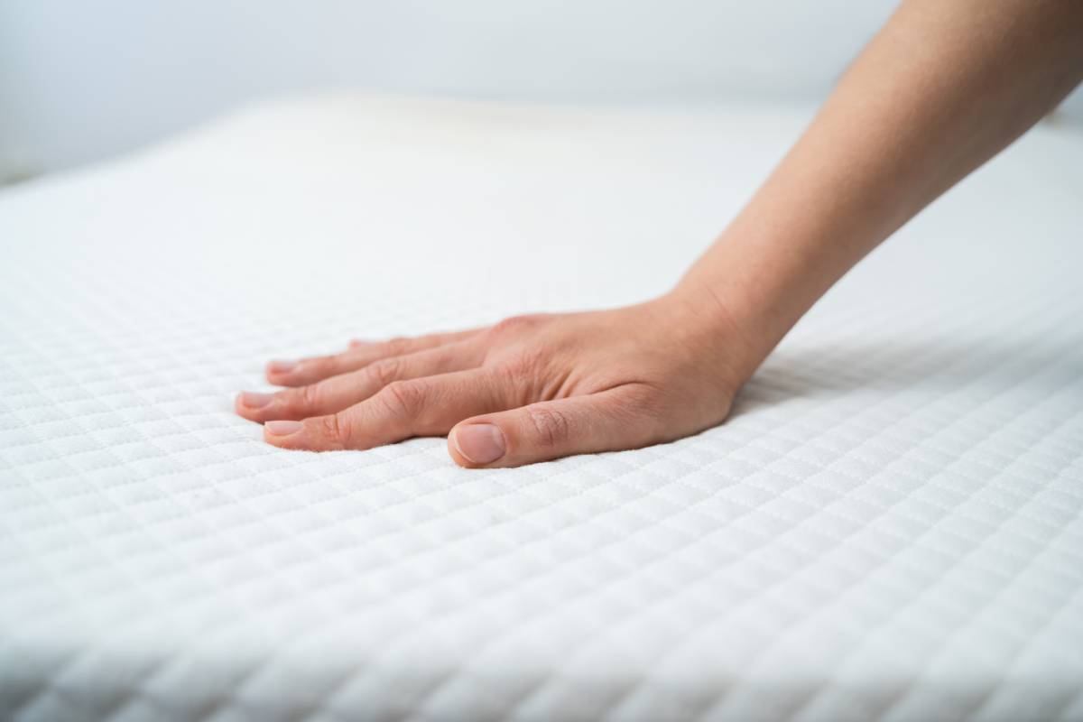 A person's hand pushing down on a twin size mattress to demonstrate softness near Florence, KY