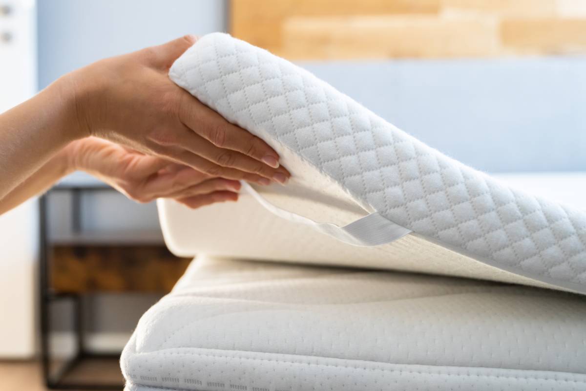 A person's hands lifting a mattress topper off the corner of a mattress near Florence, KY