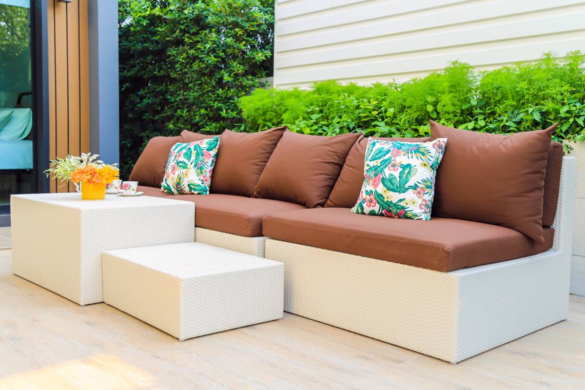 Orange outdoor sofa with throw pillows and two square ottomans.